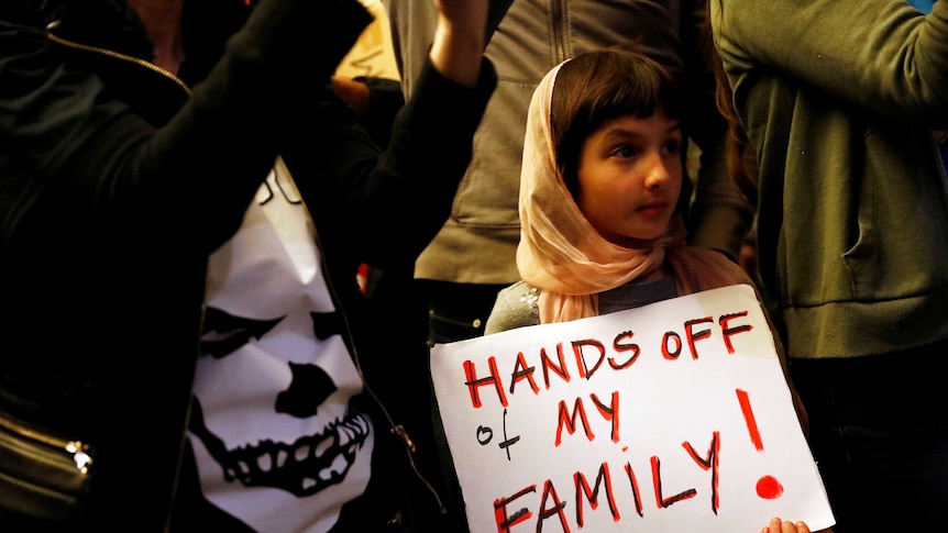 A girl holds a sign reading "Hands off my family"