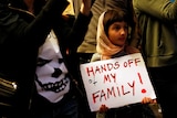 A girl holds a sign reading "Hands off my family"
