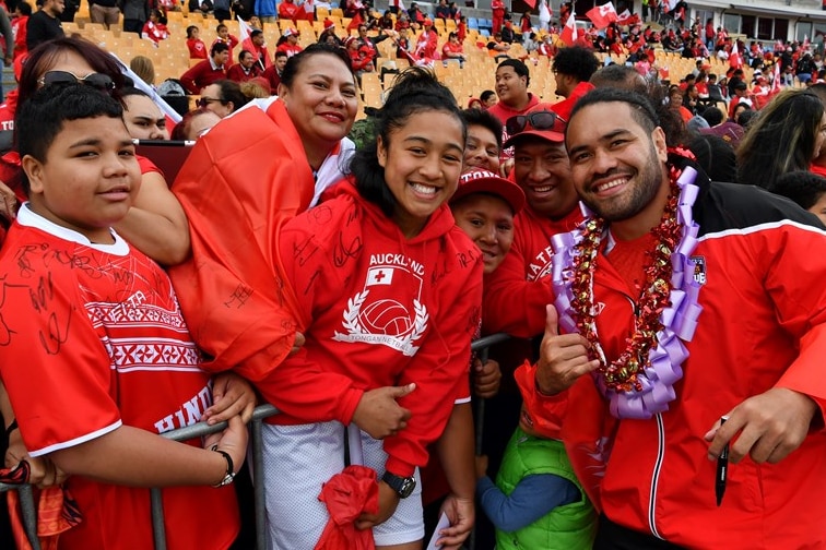 Tonga rugby player Konrad Hurrell smiles and wears a red shirt while posing with young fans after a game.