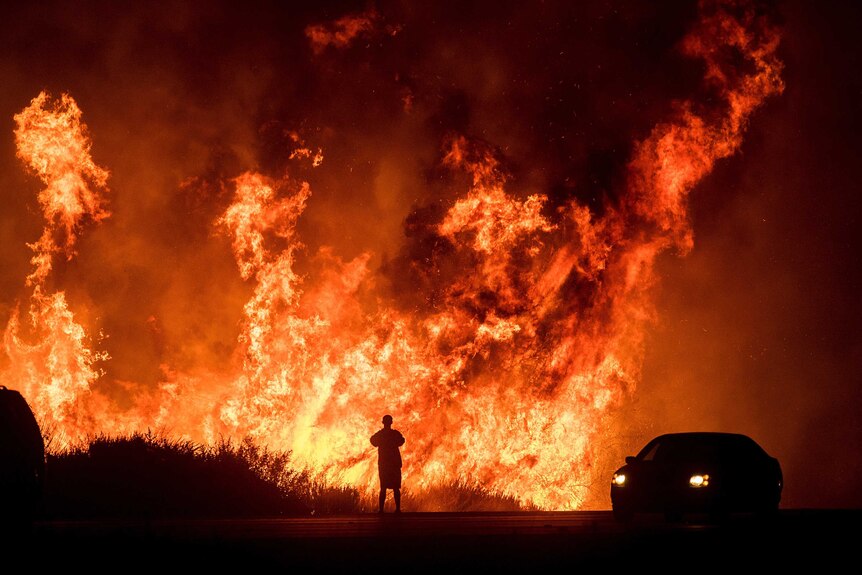 A man is silhouetted by the huge flames burning along a highway.