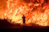 A man is silhouetted by the huge flames burning along a highway.