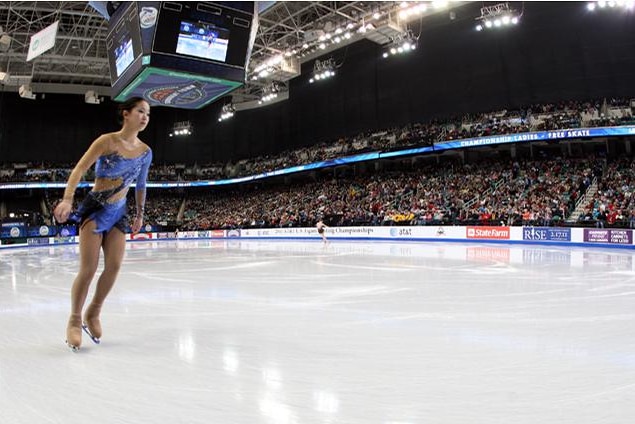 A woman ice skates in front of a stadium crowd.