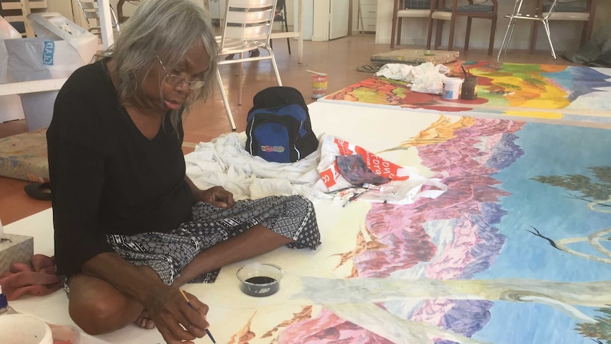 Artist Gloria Pannka paints a landscape on a giant canvas at the Many Hands Art Centre in Alice Springs