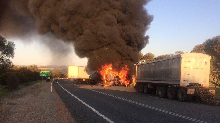 An outback highway with two trucks pulled over to the side, one is on fire