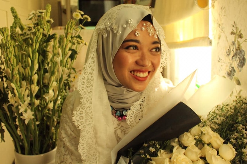 Shaffira holds is wearing her wedding gown and holds a bunch of flowers.