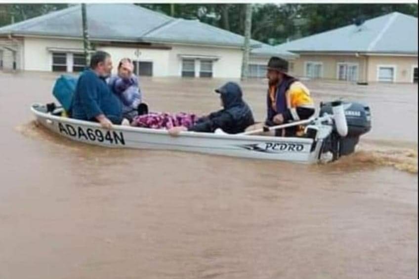 People in a boat sailing down a flooded street, with the roofs of houses in the background