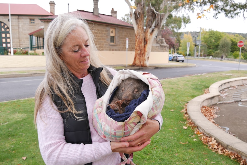 A woman holds a baby wombat outside of a jail.