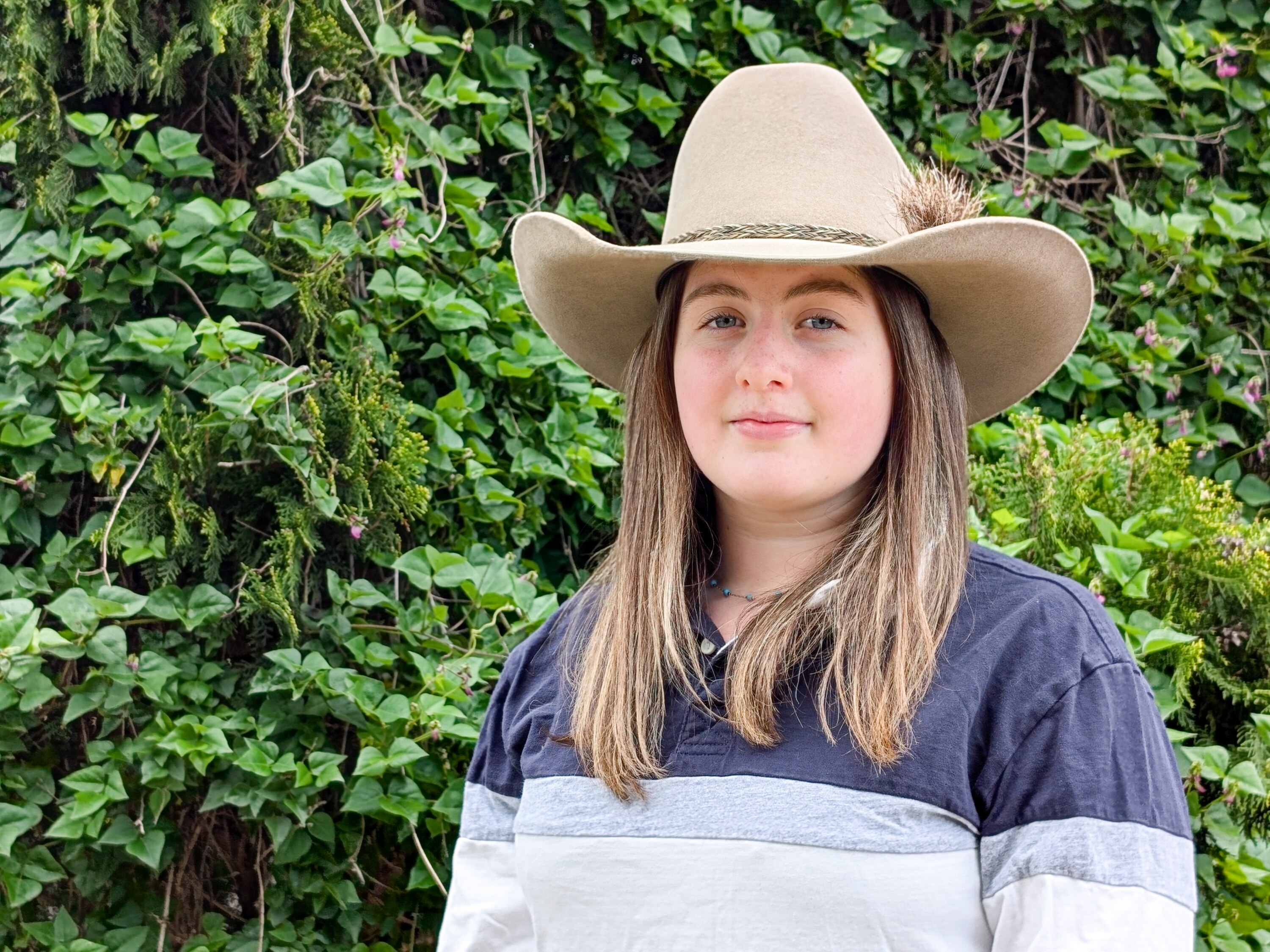 A young woman with white skin and long hair and a cowboy hat smiles at the camera