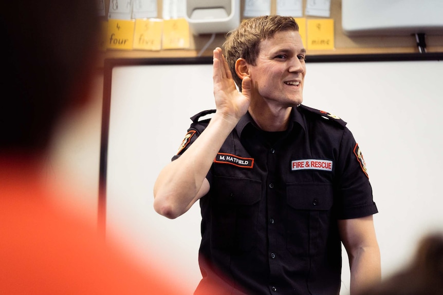 A mid shot of firefighter Michael Hatfield in a classroom at Mosman Park School for Deaf Children with his hand to his ear.