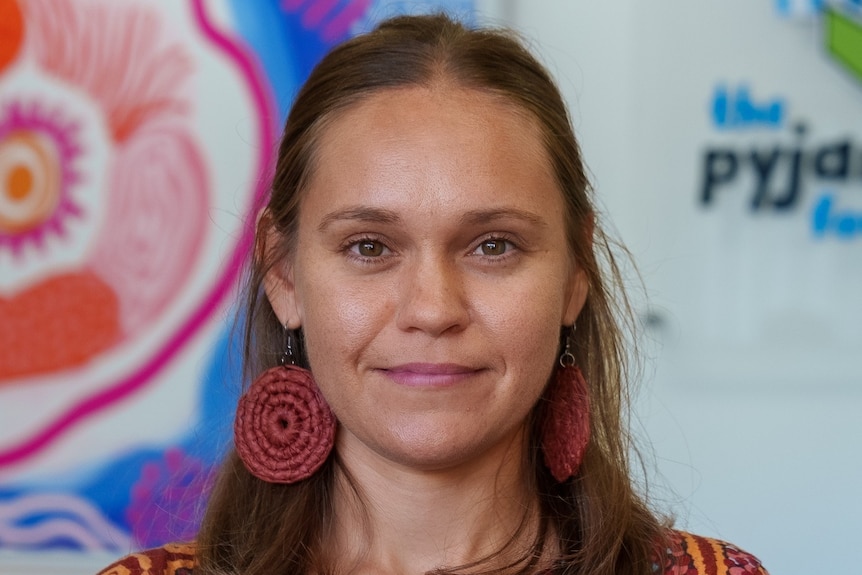 A photo of a woman wearing aboriginal art-print shirt, and red spiral shaped earings. 