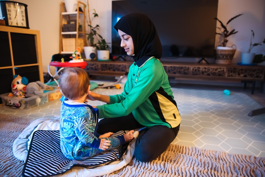 Madinah and her sibling play on the floor in a living room.