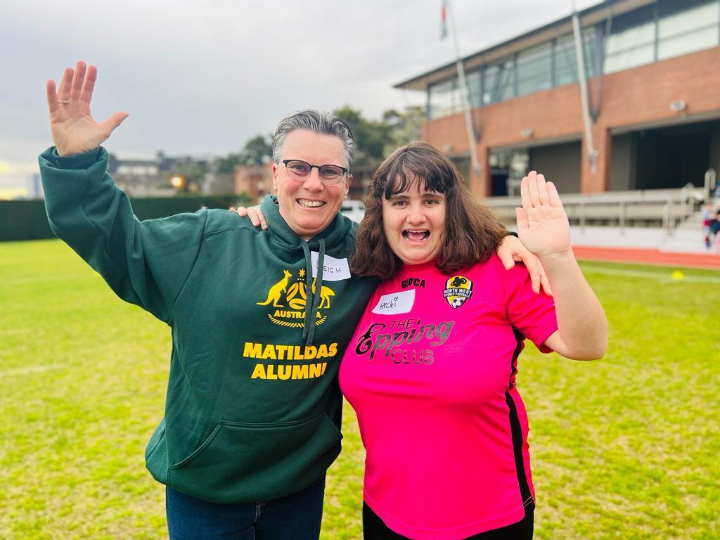 An older woman wearing a green jumper poses for a photo with a young woman wearing a pink shirt