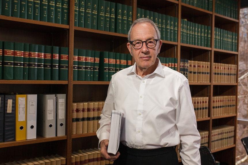 A man holding a report and standing in front of a bookshelf of legal texts.