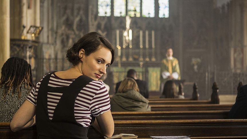 Phoebe Waller-Bridge sits in a church pew, turning around to look into the camera