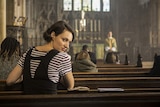 Phoebe Waller-Bridge sits in a church pew, turning around to look into the camera
