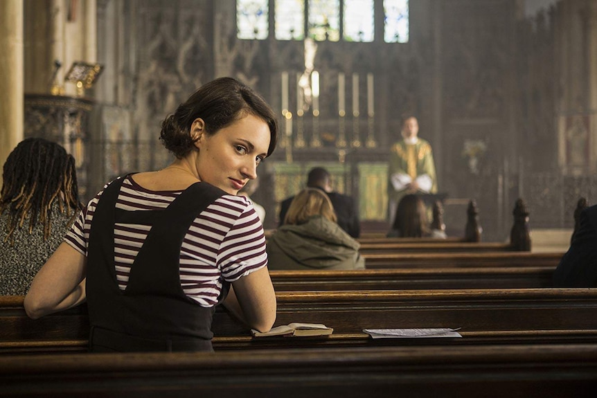 Phoebe Waller-Bridge sits in a church pew, turning around to look into the camera