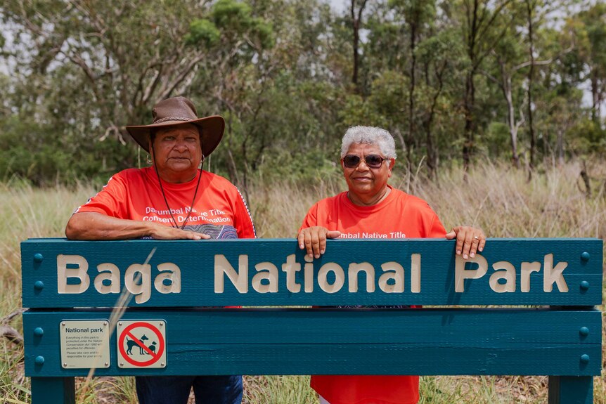 Two women standing behind Baga National Park sign in bush.