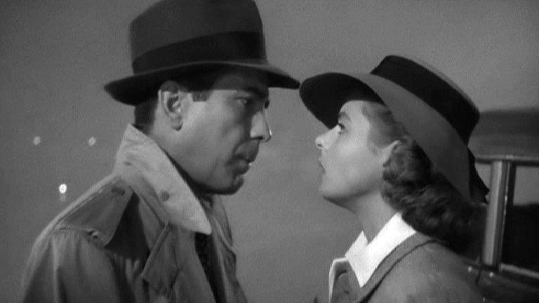 A black and white still from Casablanca, featuring a man and a woman in black hats staring intently into each other's faces.