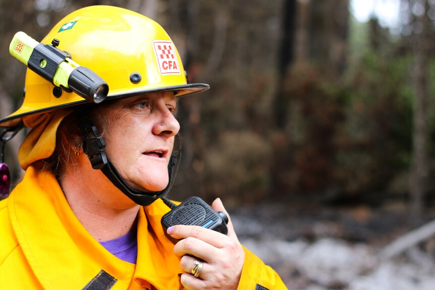 A female firefighter dressed in yellow protective gear speaking into a two way radio.