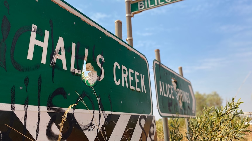 a damaged green sign saying halls creek