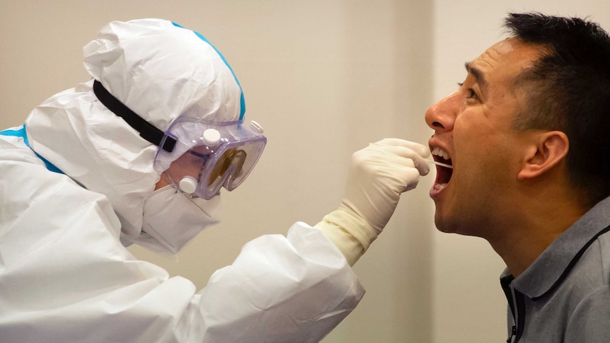 A worker in a protective suit takes a throat swab for a COVID-19