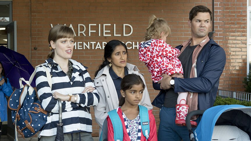 Colour still of Andrew Rannells, Aparna Nancherla and Kelly McCormack standing outside of a school in 2018 film A Simple Favour.