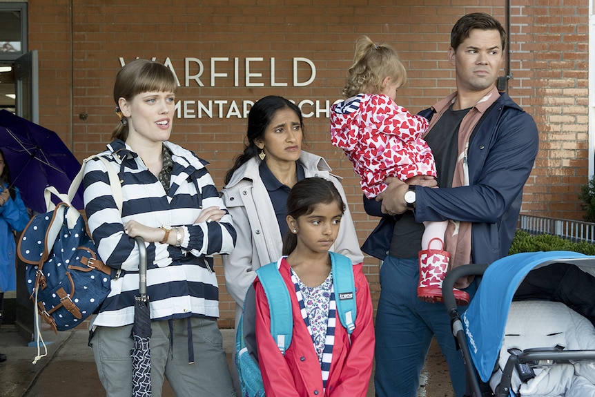 Colour still of Andrew Rannells, Aparna Nancherla and Kelly McCormack standing outside of a school in 2018 film A Simple Favour.