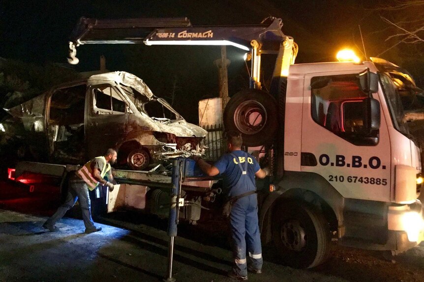 Crews load burned cars onto truck in Mati, Greece