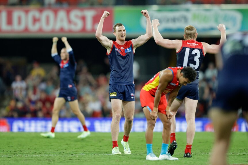 Harrison Petty and Clayton Oliver hold their arms in the air near a disappointed Suns player