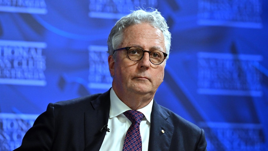 Mark Scott looks serious as he speaks, in front of a blue "National Press Club" backdrop.