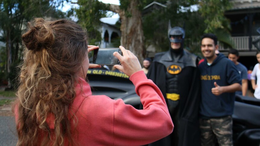 A man gets his partner to take a photo of him standing next to Batman