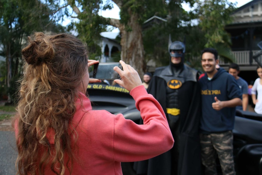 A man gets his partner to take a photo of him standing next to Batman