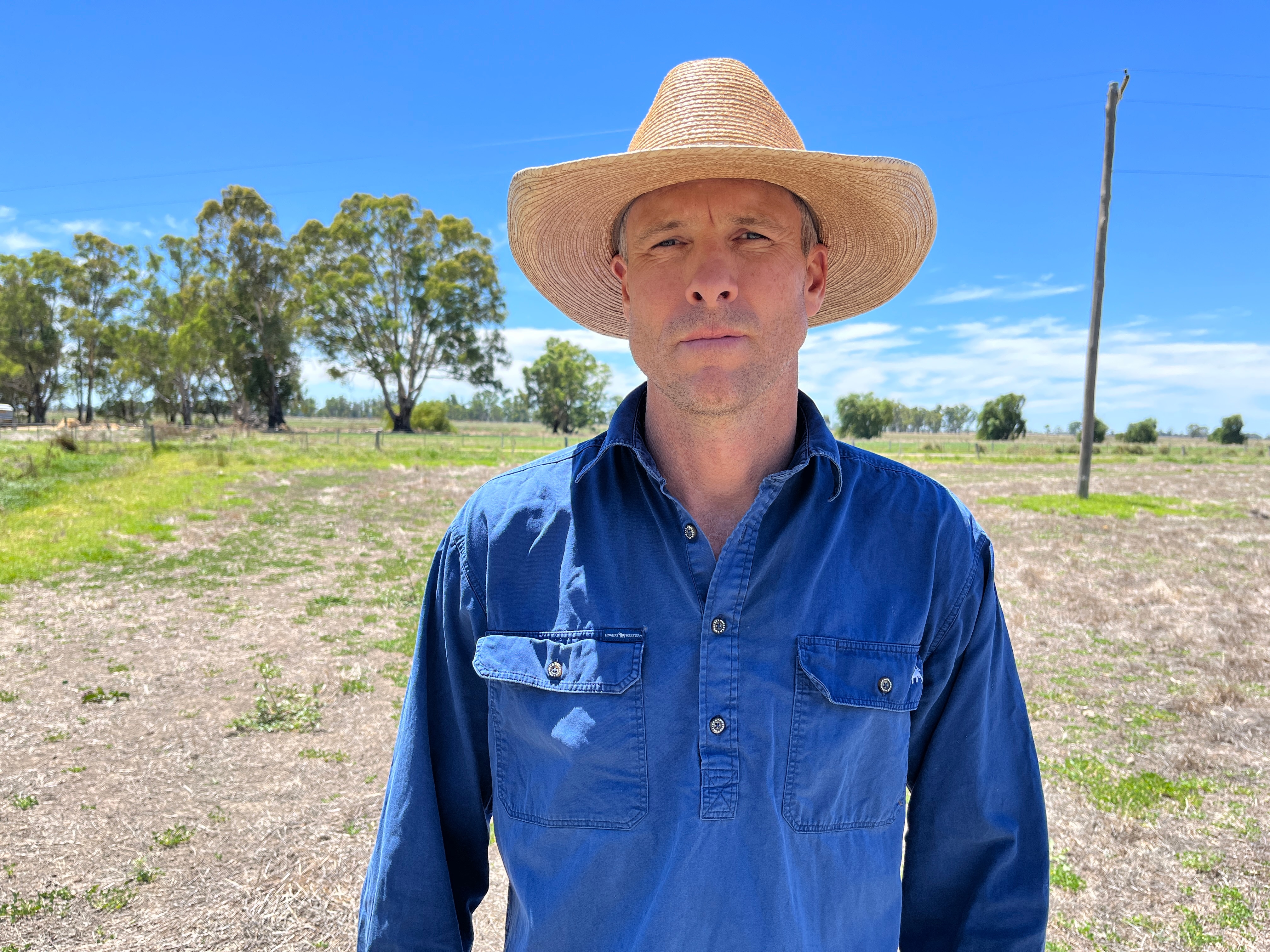 A man wearing a blue shirt and a hat looking displeased.