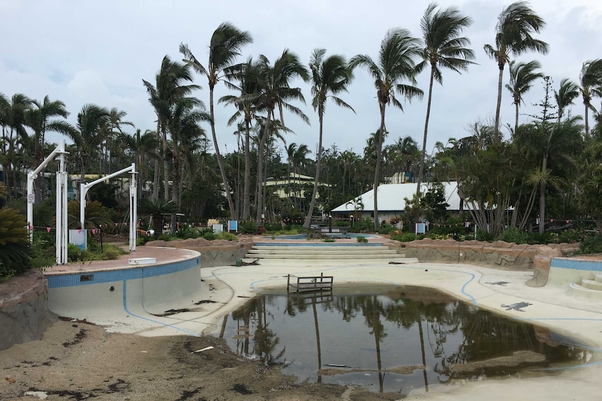 A near-empty pool complex with dirty water in the bottom