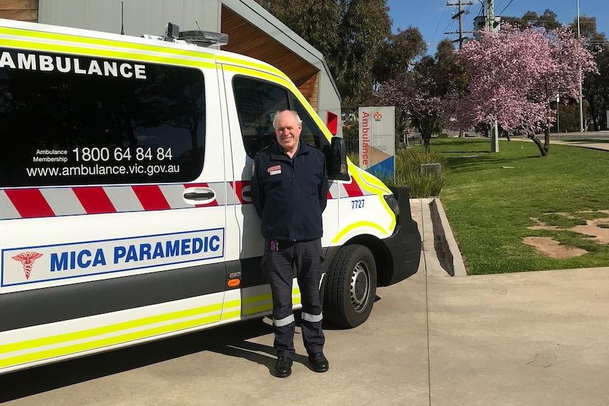 A man stands in front of a MICA ambulance on a sunny day