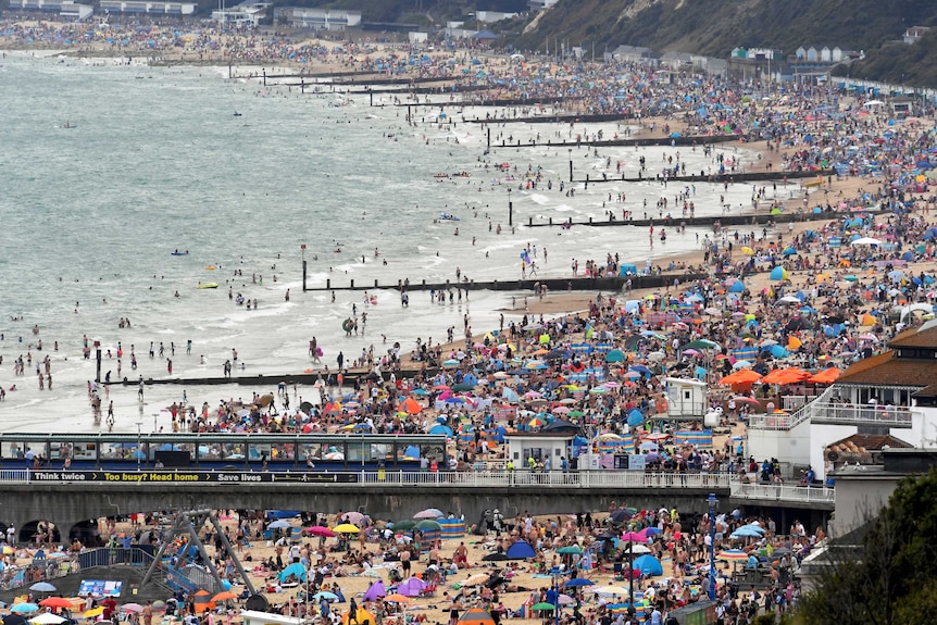 People and brightly coloured umbrellas dot a packed beach.