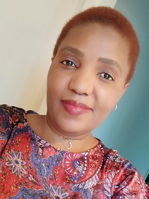 A woman with short reddish hair smiles in a tilted selfie wearing a floral shirt. 