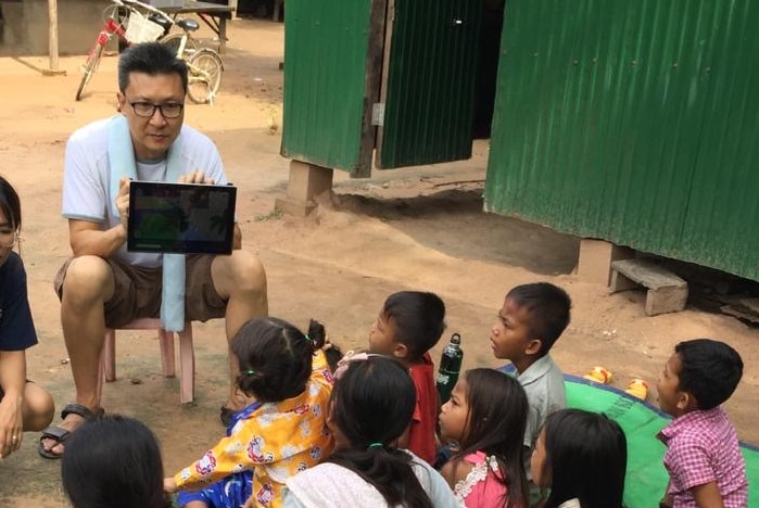 A man sitting with an iPad surrounded by small children