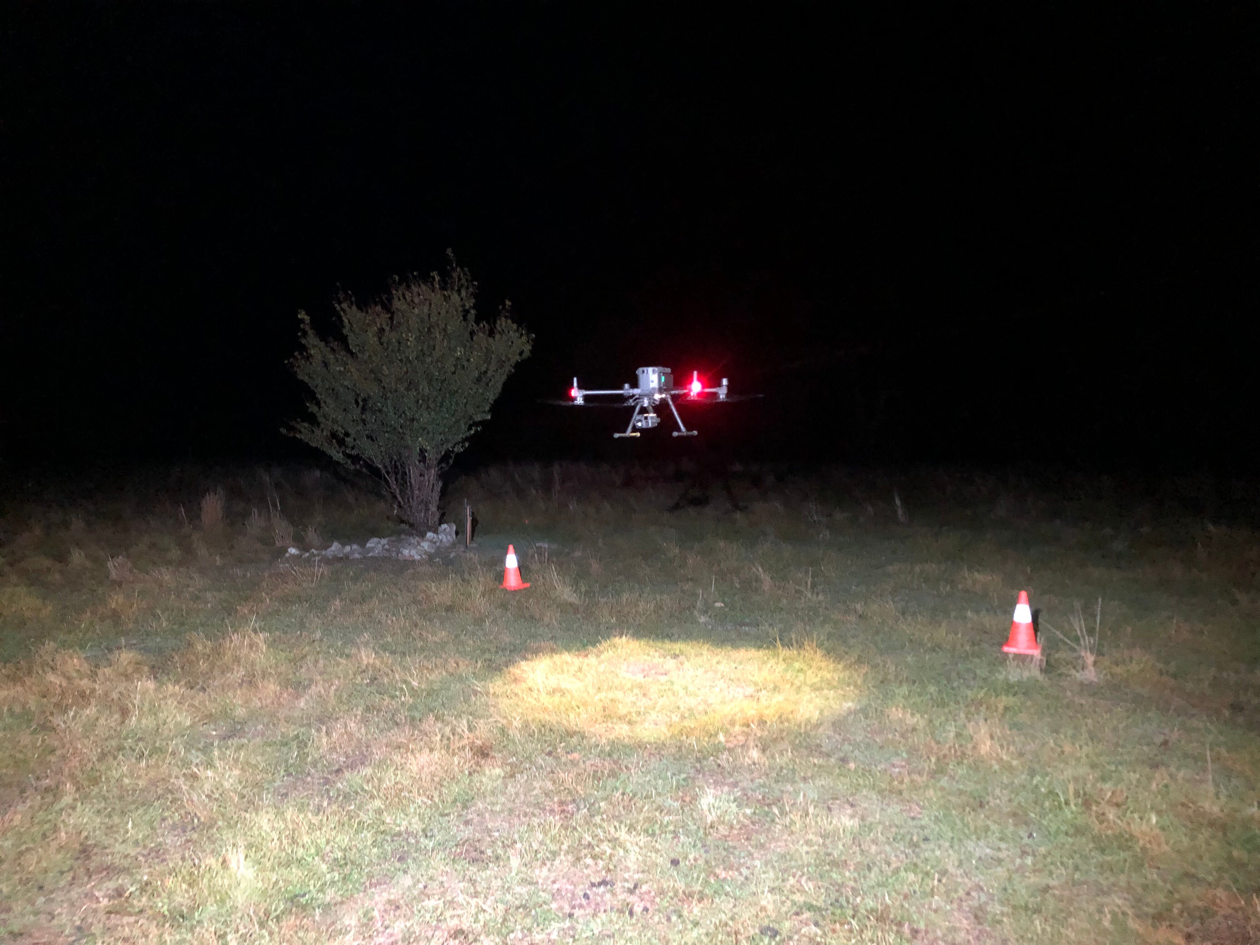 A drone flies a couple of metres off the ground in a grassy field at night.