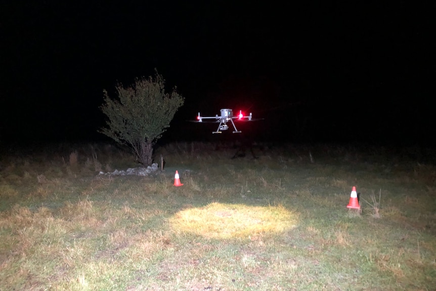 Un dron vuela a un par de metros del suelo en un campo de hierba por la noche.