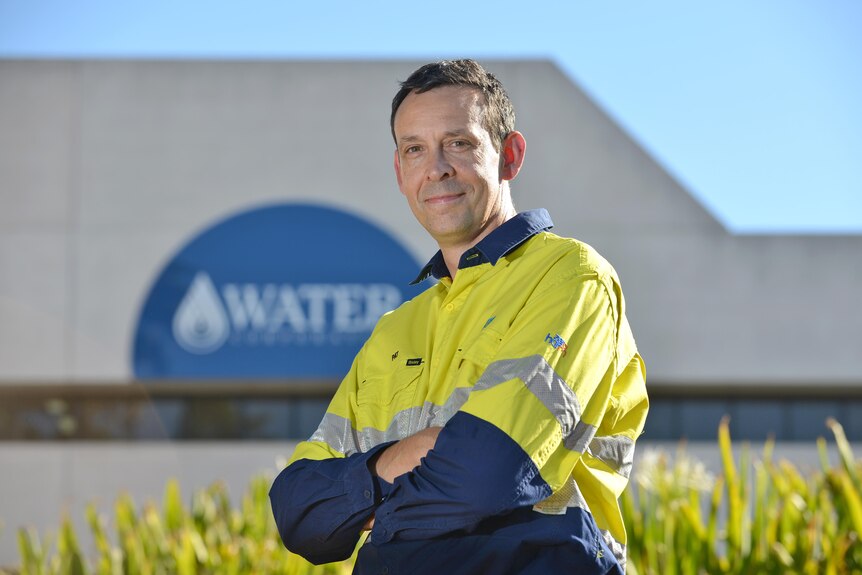 A man wearing high-vis workwear standing in front of a Water Corporation sign.  