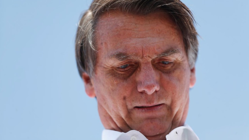 Close up of far right Brazilian presidential candidate Jair Bolsonaro, blue sky behind him, looking down pensively