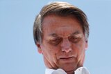 Close up of far right Brazilian presidential candidate Jair Bolsonaro, blue sky behind him, looking down pensively