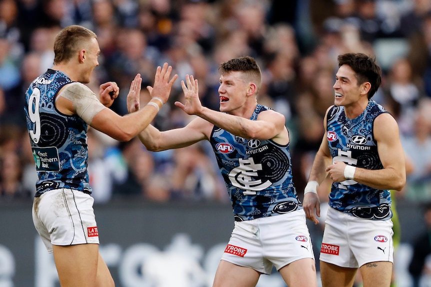 A Carlton player high fives his captain after a goal, while another smiling Blues player looks on.
