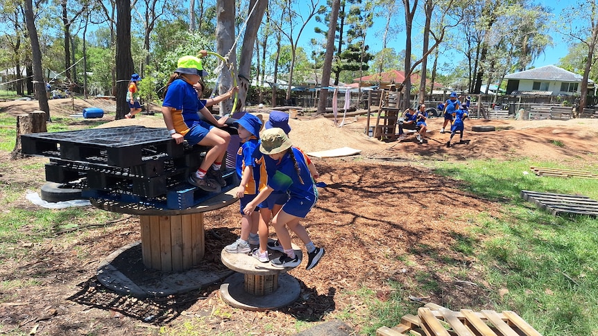 A group of kids in bucket hats balance on piles of stacked crates and wooden wheels.