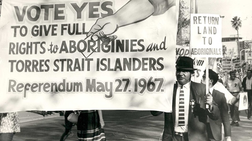 An old photo of a man holding a banner which says 'Vote Yes to give full rights to Aborigines and Torres Strait Islanders.