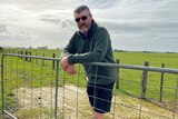Farmer leaning on metal gate with paddock in background 