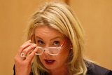 Bridget McKenzie sits at a table answering questions in a wood-panelled room