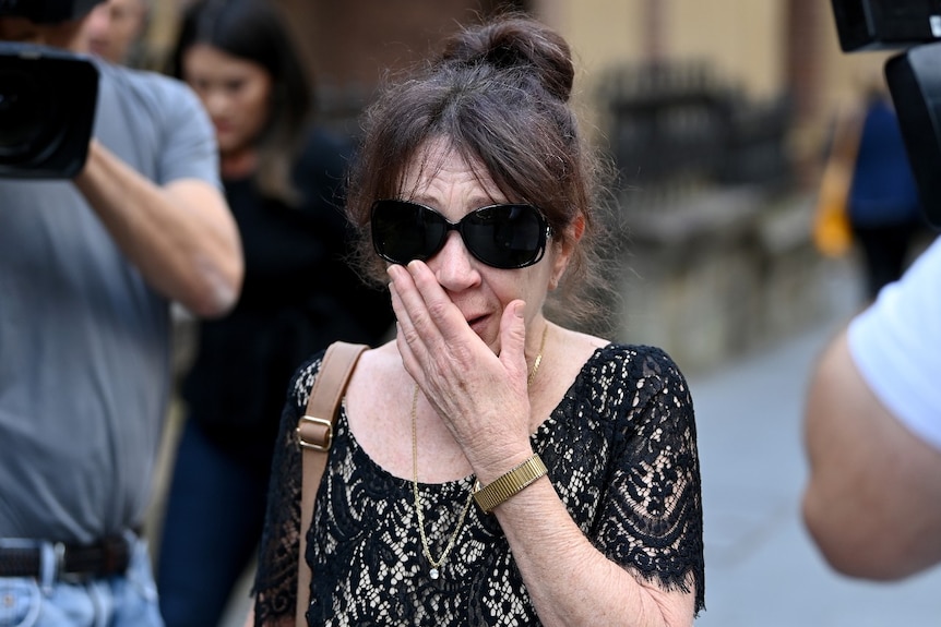A woman with large sunglasses on, covering her mouth with her hand