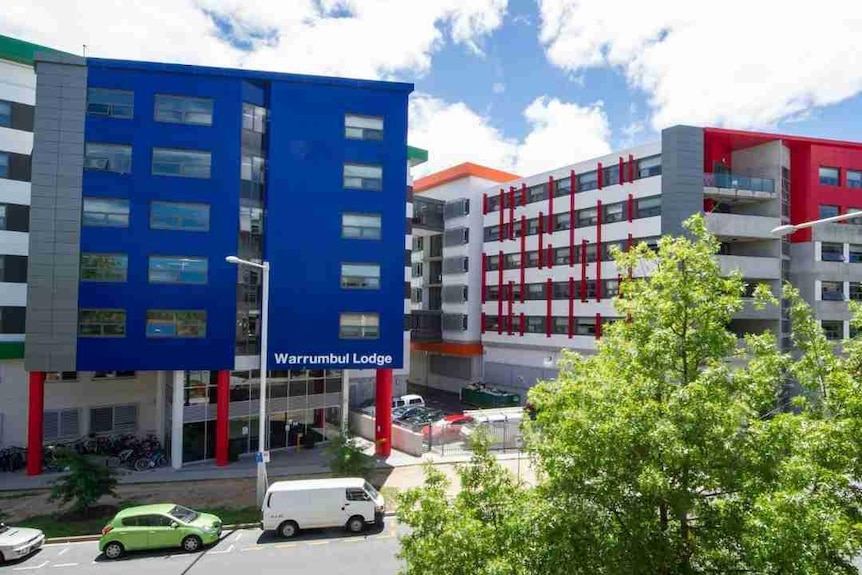 A large blue building stands with a red and gray building next to it and a sign with 'Warrumbul Lodge'